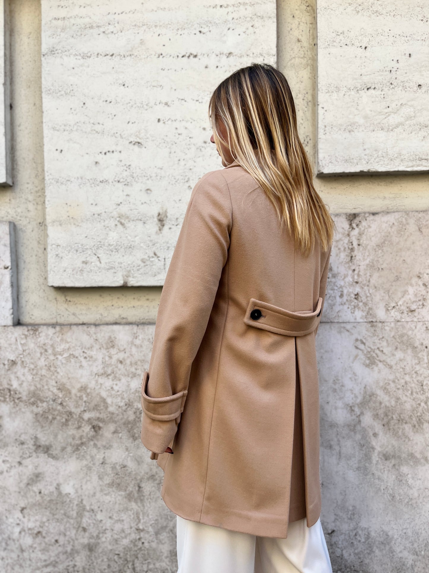 Scopri il cappotto trench Elvira color cammello di EVITA, realizzato con un pregiato mix di lana, poliammide e cashmere. Con il suo design classico e i bottoni neri, rappresenta l'artigianato italiano di alta qualità. Perfetto per un look sofisticato e senza tempo. Prodotto con passione da EVITA, made in Italy.