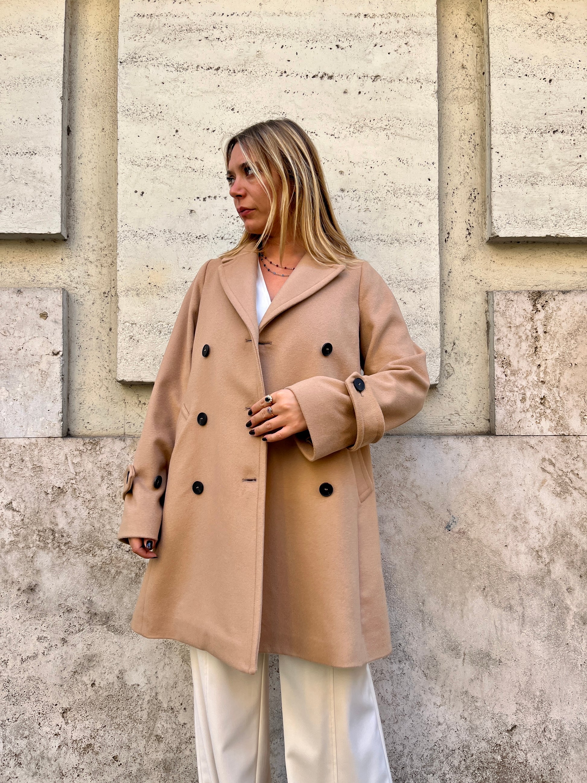 Scopri il cappotto trench Elvira color cammello di EVITA, realizzato con un pregiato mix di lana, poliammide e cashmere. Con il suo design classico e i bottoni neri, rappresenta l'artigianato italiano di alta qualità. Perfetto per un look sofisticato e senza tempo. Prodotto con passione da EVITA, made in Italy.