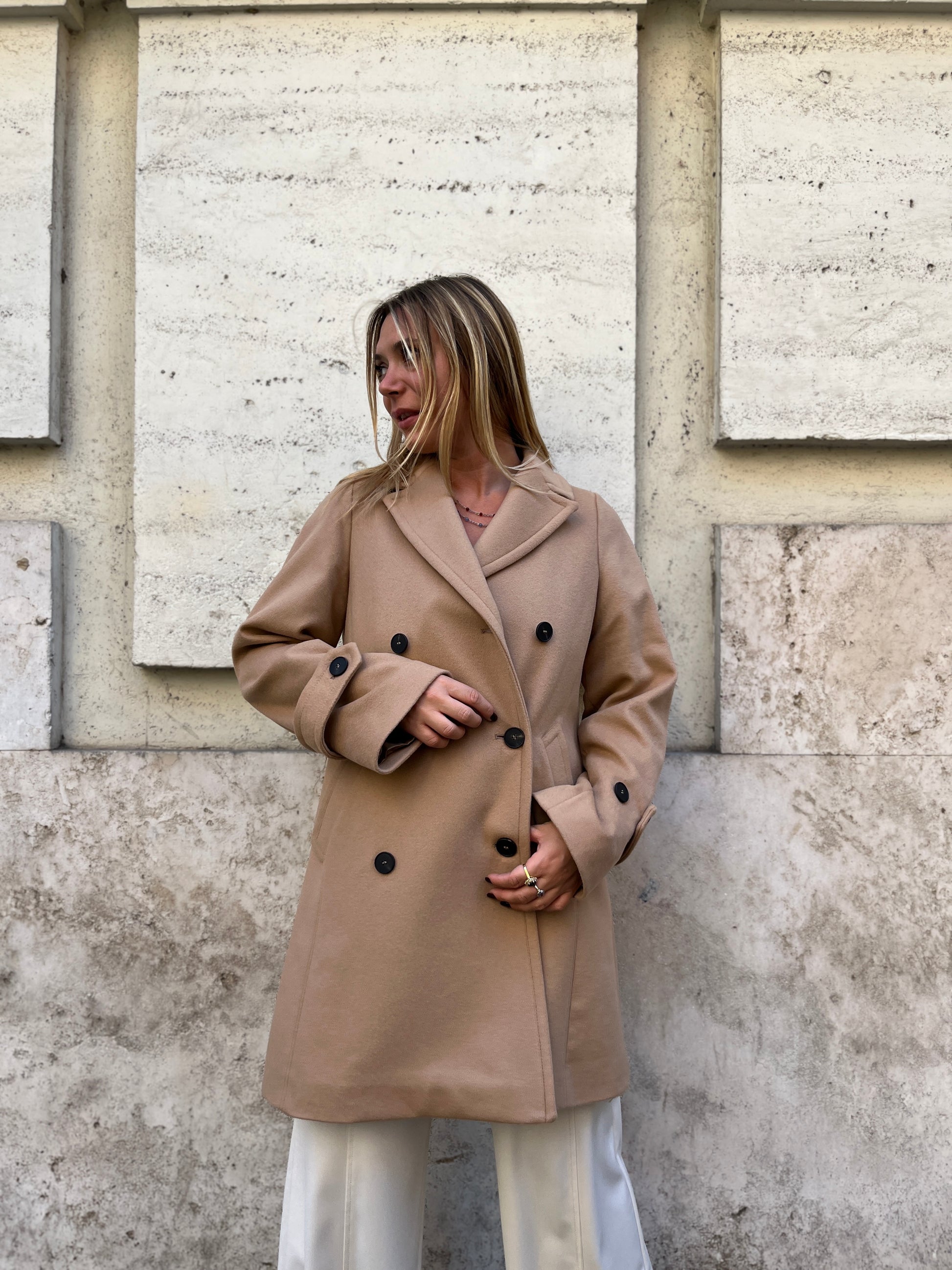 Scopri il cappotto trench Elvira color cammello di EVITA, realizzato con un pregiato mix di lana, poliammide e cashmere. Con il suo design classico e i bottoni neri, rappresenta l'artigianato italiano di alta qualità. Perfetto per un look sofisticato e senza tempo. Prodotto con passione da EVITA, made in Italy.