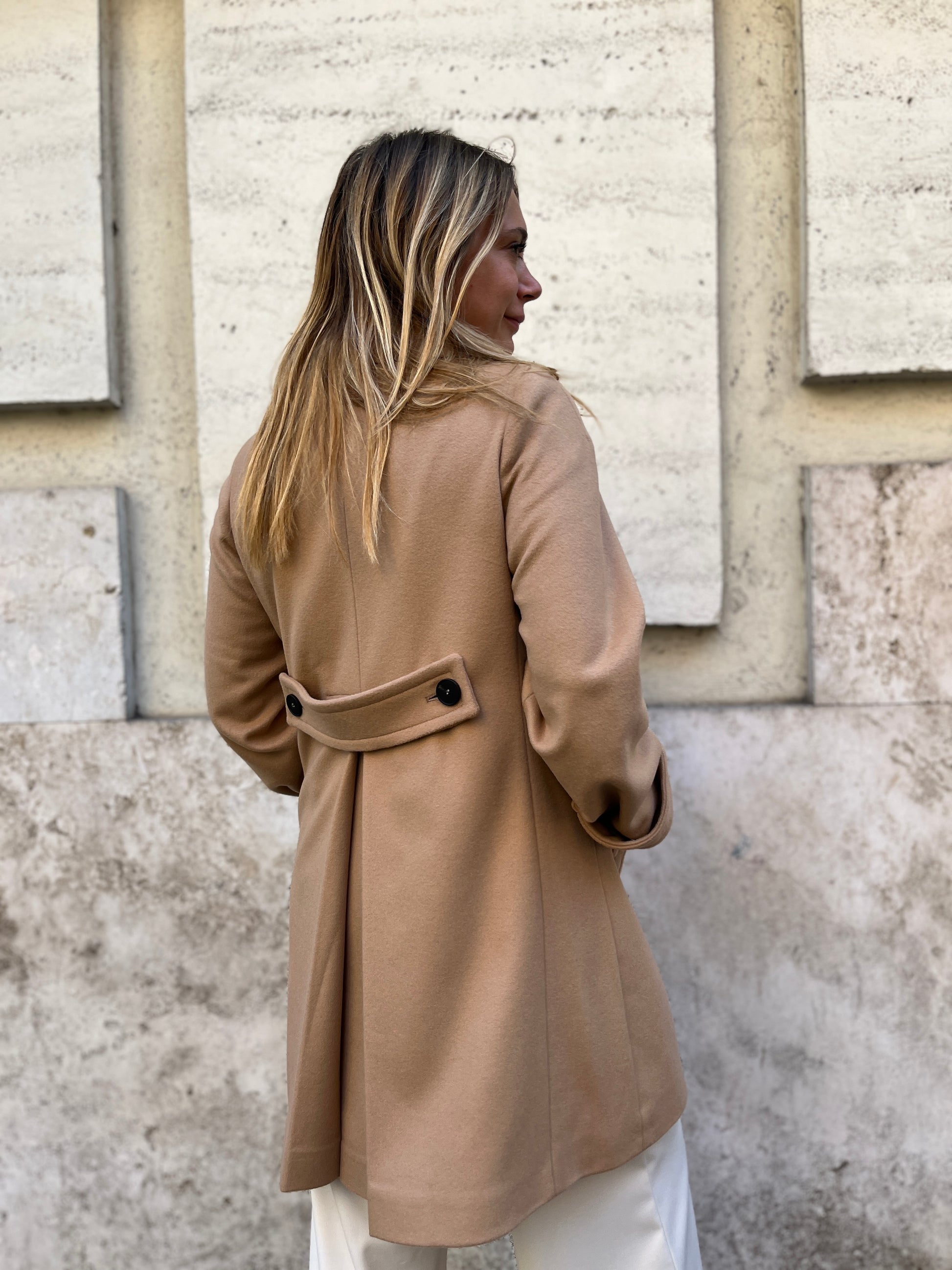 Scopri il cappotto trench Elvira color cammello di EVITA, realizzato con un pregiato mix di lana, poliammide e cashmere. Con il suo design classico e i bottoni neri, rappresenta l'artigianato italiano di alta qualità. Perfetto per un look sofisticato e senza tempo. Prodotto con passione da EVITA, made in Italy.